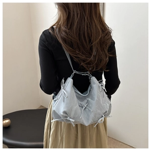 Detailed view of light blue pleated shoulder bag with decorative ribbons on a model