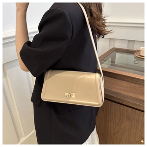 Beige tote bag with gold lock and chain strap worn by a model in a modern home setting