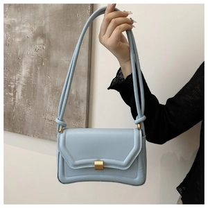 Close-up of light blue saddle bag with gold metal clasp and knotted shoulder strap