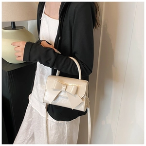 Detail showing cream glossy bow handbag with metallic texture and adjustable shoulder strap