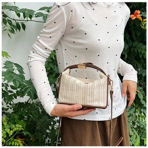 Fashionable straw crossbody bag with brown leather trim shown on model against nature background