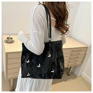 Detail of black pleated bucket bag with silver metal butterflies and slender shoulder straps