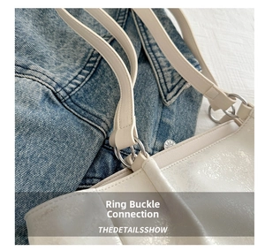 Close-up of metal ring buckle and stitching on white leather shoulder bag strap