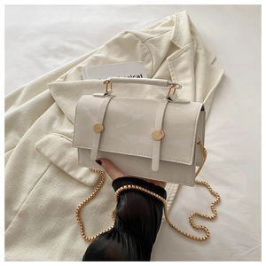 Detail of white patent leather crossbody bag with gold hardware and chain strap