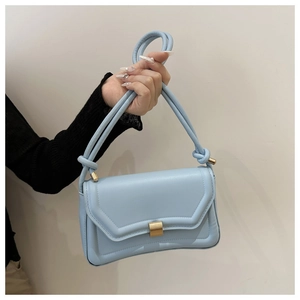 Detail of light blue crossbody saddle bag with gold buckle and knotted top handle