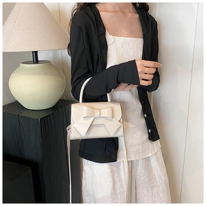 Detail of cream white handbag with bow decoration and glossy finish on textured leather