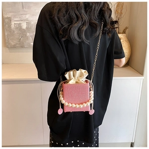 Pink woven bucket bag with pearl handle and chain strap worn as a crossbody bag