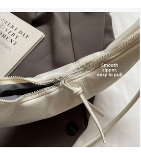 Detail of silver smooth zipper and cream leather on minimalist crescent crossbody bag