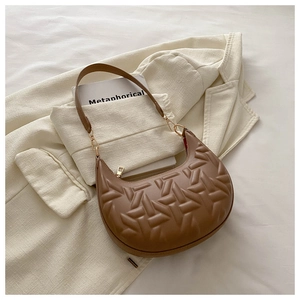 Detail of a brown crescent shoulder bag with geometric quilting on a beige blazer background