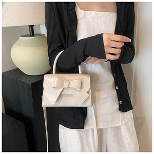 Detail of cream white bow handbag showing polished finish and top handle design