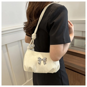 Detail of cream shoulder bag featuring silver bow accent and decorative bead knot strap