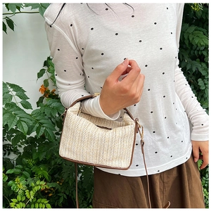 Detail of straw woven shoulder bag with brown leather trim against green foliage background