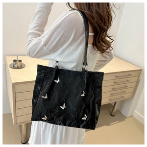 Detail of black tote bag featuring silver butterfly ornaments and textured leather finish