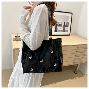 Detail of black pleated bucket bag with silver butterfly charms worn by a model