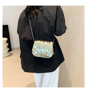 Close-up of a glittering sequin crossbody bag with a metal chain strap on a model