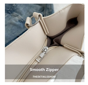 Detailed close-up of smooth silver metal zipper on cream white faux leather tote bag