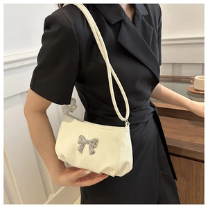 Detail of cream fabric shoulder bag with silver metallic bow and textured surface