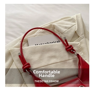 Close-up of red patent leather shoulder bag with knot detail handle and silver metal ring