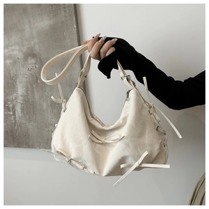 Detailed close-up of cream shoulder bag featuring textured fabric and bow ribbon accents