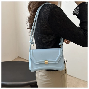 Detail of light blue saddle bag with gold metal clasp and knotted strap on shoulder