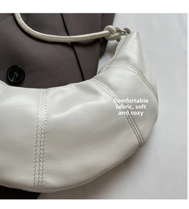Detail view of beige crescent bag featuring soft pleated fabric and knotted strap