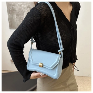 Close-up of a light blue minimalist saddle bag with matte gold buckle worn by a model