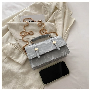 Detail of grey marble textured handbag with gold chain strap on a white blazer