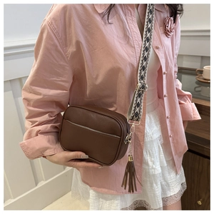 Brown lychee leather crossbody bag featuring geometric woven strap and leather tassel detail