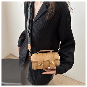 Detail of warm khaki square bag featuring floral jacquard strap and dual metal buckles