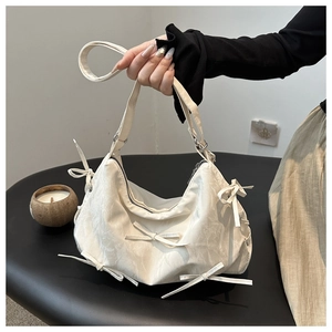 Detail of cream pleated handbag featuring decorative bows and silver metallic zipper
