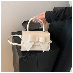 Detailed view of the cream white bow knot handbag held with a stylish top handle