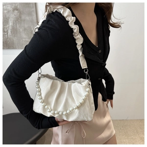 Close-up of cream pleated shoulder bag with pearl chain and elegant faux leather texture