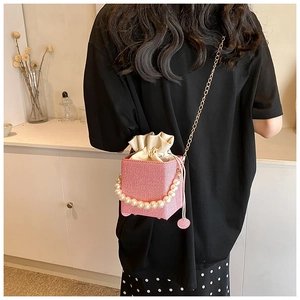 Pink drawstring bucket bag with pearl handle and metal chain shown on person