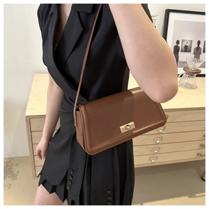 Brown matte leather shoulder bag detail with gold clasp and slim strap on model