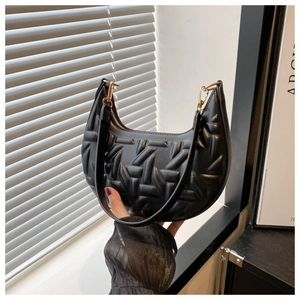 Detail of black quilted hobo bag with geometric texture, gold hardware and red lining