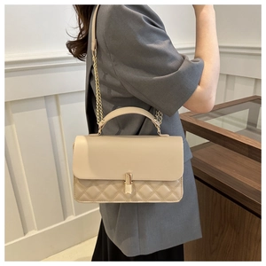 Detailansicht der beigen gesteppten Handtasche mit Goldkette am weiblichen Modell