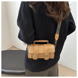 Detail of caramel cylinder bag with gold rivets and colorful geometric strap on model