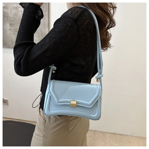 Model showing a light blue leather saddle bag with a gold buckle and elegant knot strap