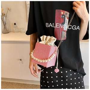 Detail of pink woven bucket bag with large pearl handle and golden chain strap detail