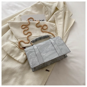 Detail of grey marble texture crossbody bag with gold chain and handle on beige suit