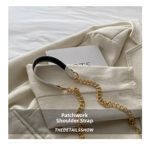 Detail of a bicolored leather shoulder strap with bold gold chain and white stitching