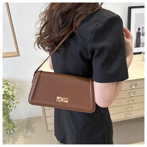 Brown leather crossbody bag with gold twist-lock closure shown in a lifestyle setting