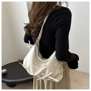 Close-up of soft beige shoulder bag featuring decorative bows and elegant textured finish