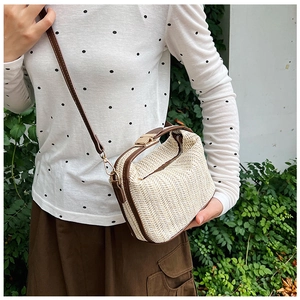 Close-up of a woven straw shoulder bag with dark brown leather trim and golden hardware