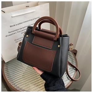 Detail of a black and brown crossbody bag with unique wooden round handle and gold rivets