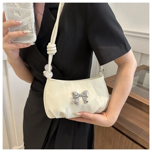 Detail of cream white pleated shoulder bag featuring a silver bow and beaded strap