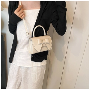 Detail shot of a beige bow-tie crossbody bag with matte faux leather and silver hardware