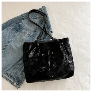 Detail of black glossy tote bag featuring pleated texture and bow strap design