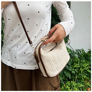 Detailed view of woven straw shoulder bag with dark brown leather trim and golden clasp