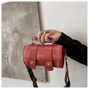 Detail of red cylindrical faux leather bag with vintage texture and gold twist lock